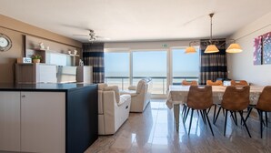 A modern hotel room with a kitchen area, a dining table with chairs, a sofa, and a view of the ocean. - Apartment With a top Location in Mariakerke (Ostend)