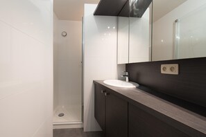 A modern bathroom with a glass shower enclosure, a white sink, and dark wooden cabinetry. - Apartment With a top Location in Mariakerke (Ostend)