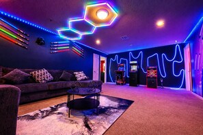 A room with a sofa, a coffee table, arcade games, and neon lights. - Themed retreat w/ pool, arcade & resort access (Kissimmee)