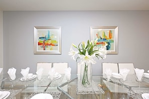 Une salle de conférence avec une table en verre, des chaises blanches et un vase rempli de fleurs blanches.