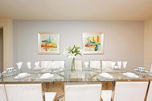 Un coin repas avec une table en verre, des chaises blanches et un vase de fleurs.