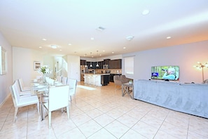 A spacious living area with a dining table, chairs, a kitchen in the background, and a television on the right.