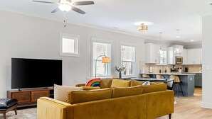 A modern living room with a sofa, a flat-screen TV, and a ceiling fan. - Family-Friendly 4BR w/ Fenced Yard & Parking (Durham)