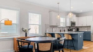 A modern kitchen with white cabinets, a central island, and a dining area with a round table and chairs. - Family-Friendly 4BR w/ Fenced Yard & Parking (Durham)