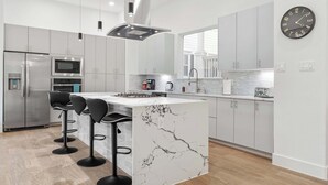 A modern kitchen with a marble island, stainless steel appliances, and bar stools. - Luxury 3BR 3BA Home with Parking & Downtown Views (Houston)