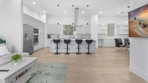 A modern kitchen with white cabinets, a central island with bar stools, and a dining area with a table and chairs. - Luxury 3BR 3BA Home with Parking & Downtown Views (Houston)