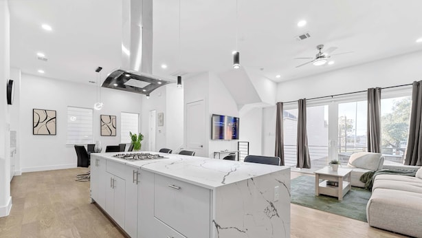 A modern kitchen with a white marble island, a dining area with a sofa, and a large window with curtains. - Luxury 3BR 3BA Home with Parking & Downtown Views (Houston)