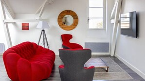 A modern living room with a red bean bag, a grey armchair, a tripod lamp, and a round mirror on the wall. - Artists' Loft (Sainte-Savine)