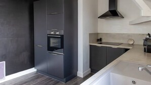 A modern kitchen with dark cabinetry, a built-in oven, and a stainless steel sink. - Artists' Loft (Sainte-Savine)