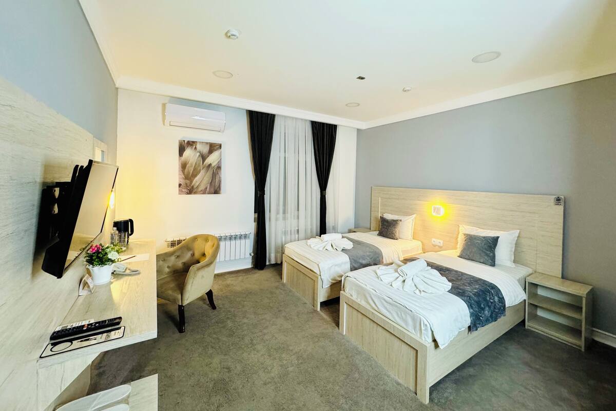 Une chambre d’hôtel avec deux lits, un bureau avec une chaise, une machine à café et un téléviseur fixé au mur.