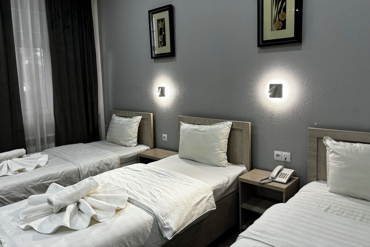 Une chambre d’hôtel avec trois lits, chacun étant équipé de draps et d’oreillers blancs. On y trouve deux appliques murales et une table de chevet avec un téléphone sur le côté.