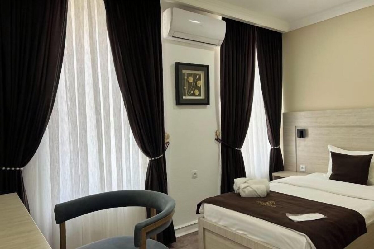 A hotel room with a bed, a chair, a door, and curtains.