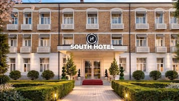 Un hôtel à la façade symétrique, doté de nombreux balcons et d’une entrée centrale agrémentée d’un tapis rouge.