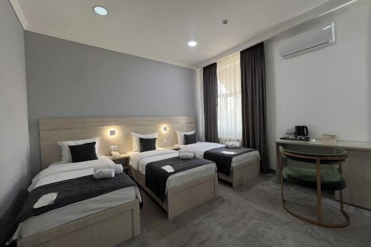 A hotel room with two beds, a small table, and a window with curtains.