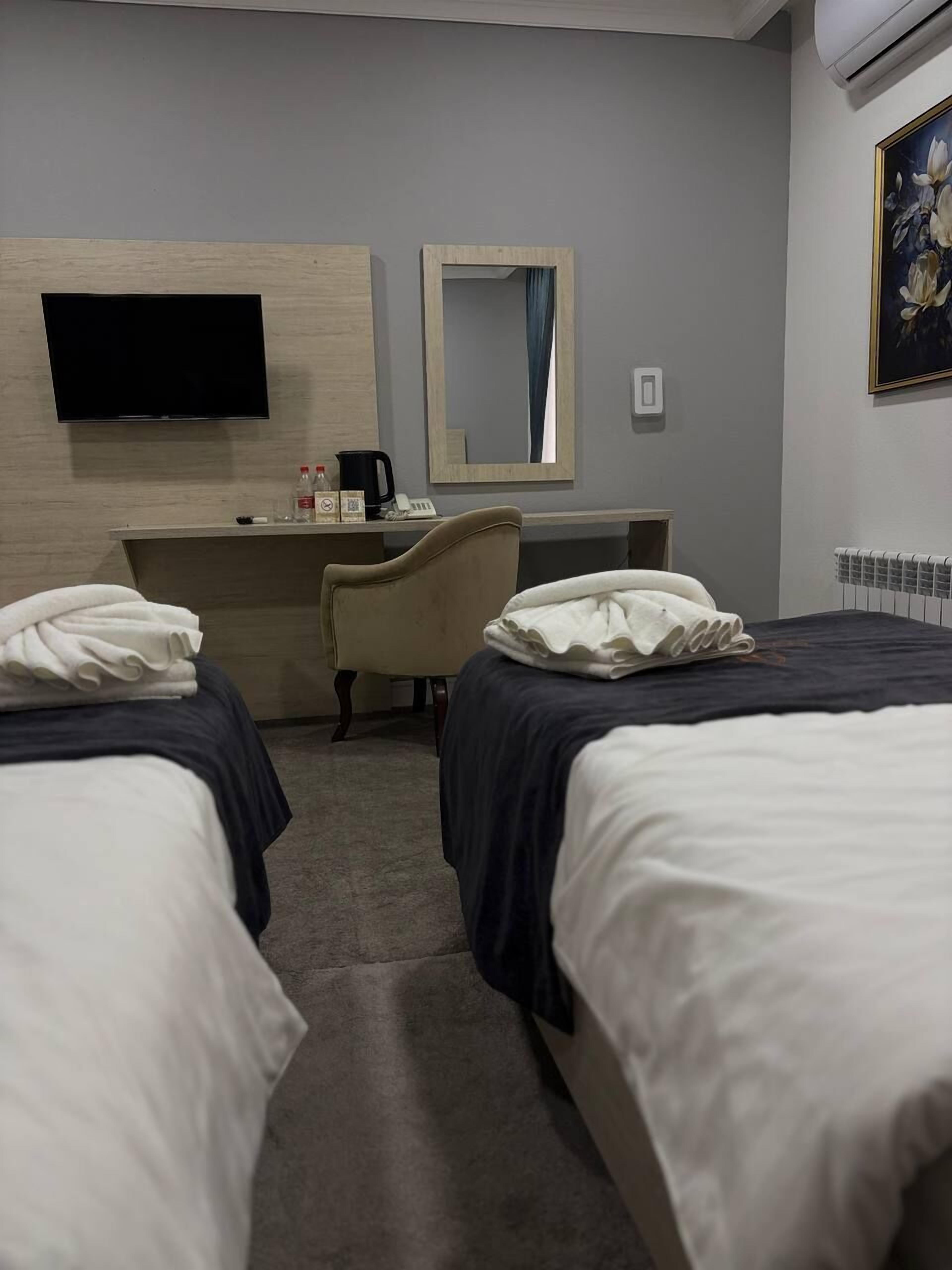 A hotel room with two beds, a desk, a chair, a flat-screen TV, a mirror, and a radiator.