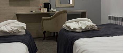 A hotel room with two beds, a desk, a chair, a flat-screen TV, a mirror, and a radiator.
