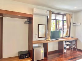 Una habitación con escritorio de madera, televisor, refrigerador pequeño y una silla.