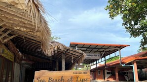 Een houten bordje met 'Sea Beach at Lipe', met een rieten dak en een overdekt gedeelte op de achtergrond.