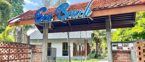 A building with a sign that reads 'Sea Beach' and a covered walkway leading to the entrance.