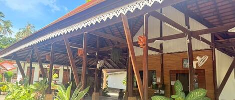 A covered outdoor area with a wooden structure, potted plants, and a clear sky.