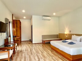 A hotel room with a bed, a TV, a wooden wardrobe, a bench, and an air conditioning unit.