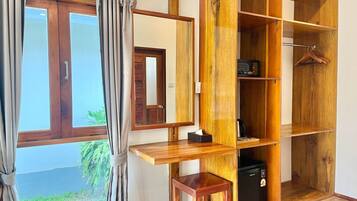 A room with a wooden desk, a small stool, a wardrobe with multiple shelves, and a hanging rack.