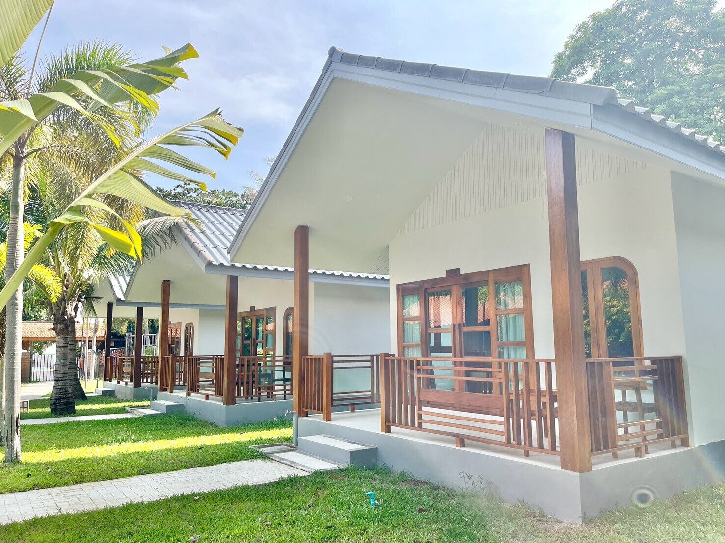 A two-story building with a covered porch and a small garden area with palm trees.