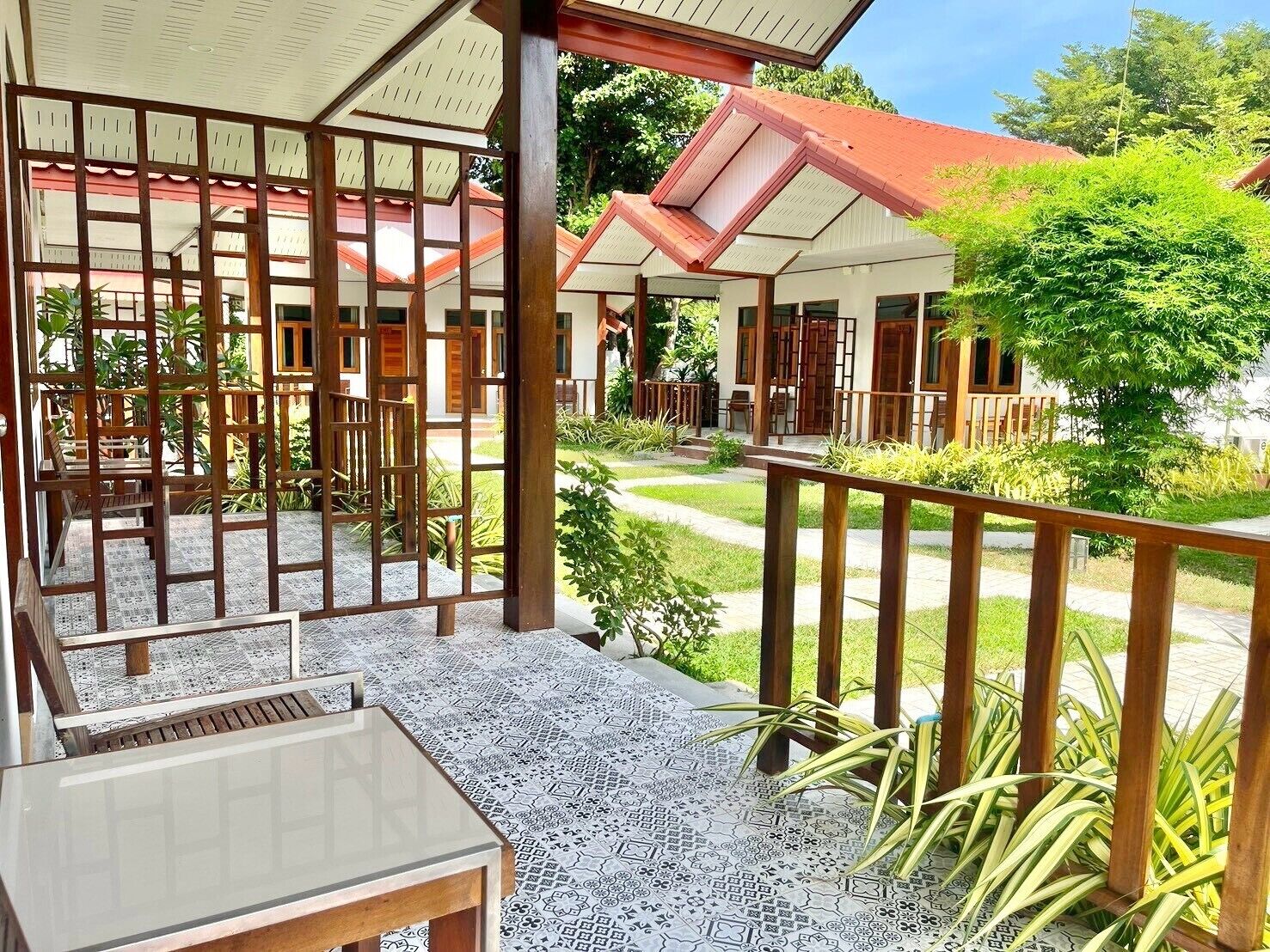 A covered outdoor seating area with a patterned floor, wooden furniture, and a view of a building with a red roof.