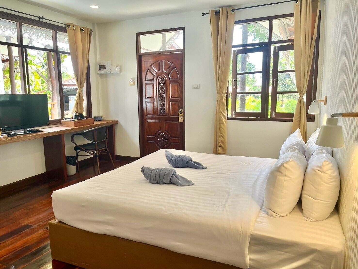 A hotel room with a bed, a desk, a television, and a door.