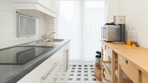 A compact kitchen with a black countertop, stainless steel sink, and a microwave. There is a wooden table with a basket and a trash can. - Cozy Apartment Near the Beach (Ostend)