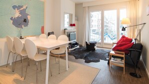 A modern living room with a dining area, a large map on the wall, a television, and a view of the city through large windows. - Cozy Apartment Near the Beach (Ostend)