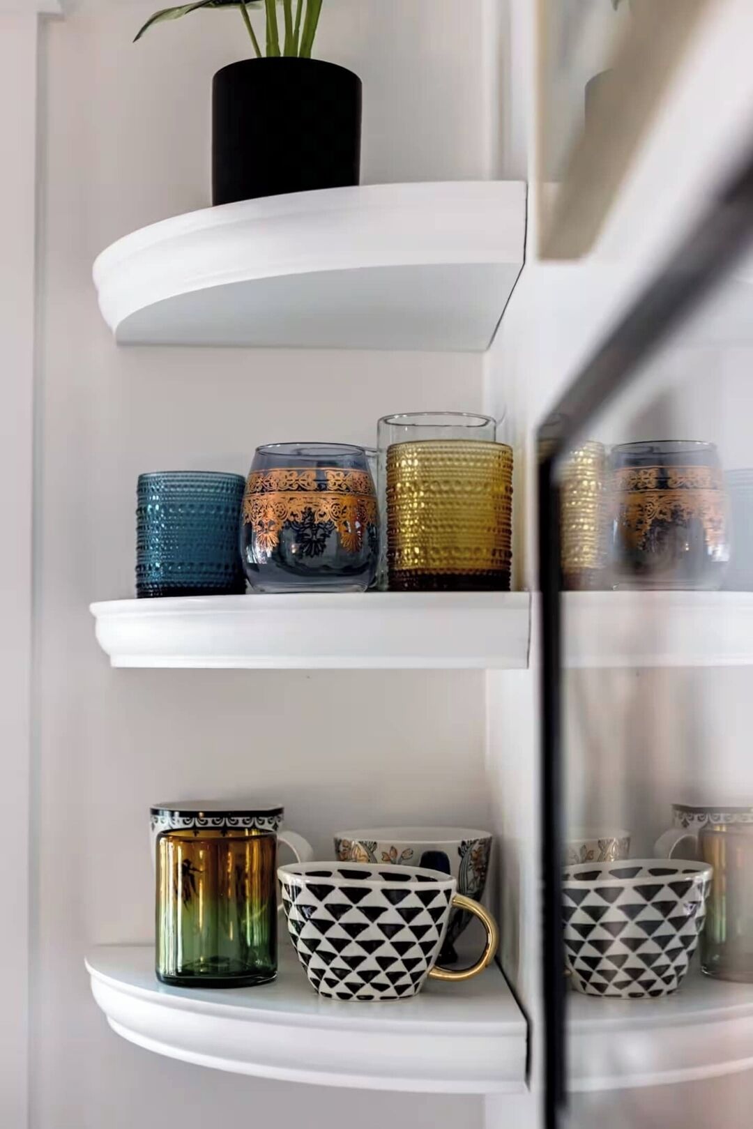 A white shelf with decorative glassware and patterned mugs.