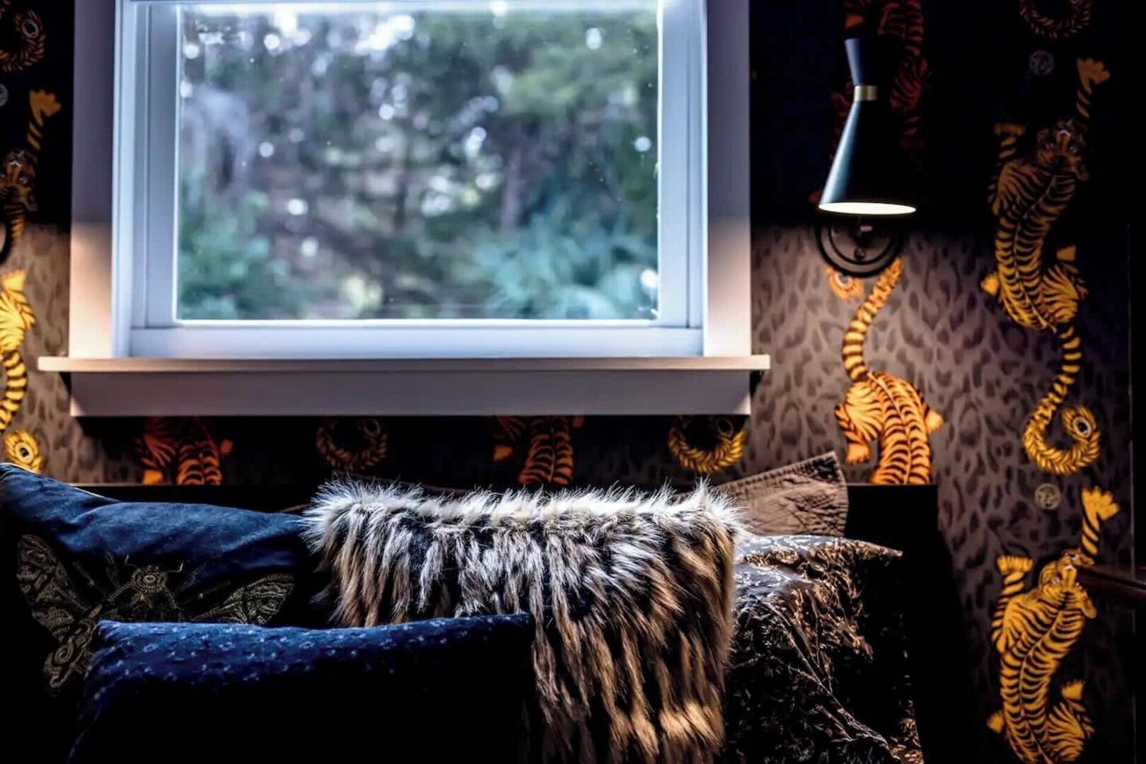 A room with a window, patterned wallpaper, a fur throw, and a lamp.