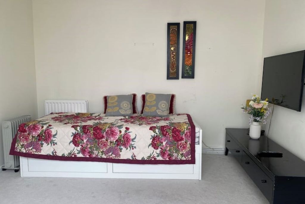 Een slaapkamer met een bed, twee aan de muur bevestigde fotolijstjes, een radiator, een dressoir en een televisie.