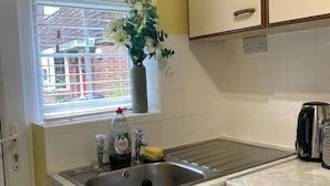 Une cuisine dotée d’un évier en acier inoxydable, d’une fenêtre donnant sur des immeubles, d’un vase rempli de fleurs et d’une bouilloire posée sur le plan de travail.