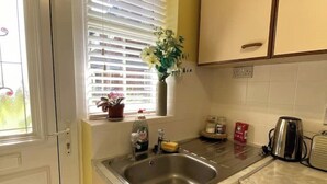 A kitchen with a stainless steel sink, a window with blinds, a vase with flowers, and a kettle on the counter. - Cosy 1 Bedroom Apartment Private Access in Guildford

 (Guildford)