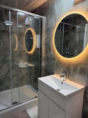 A modern bathroom with a glass-enclosed shower, a round mirror with underglow lighting, and a white sink with a chrome faucet.