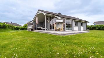 A modern house with a covered patio, a dining area, and a large lawn.
