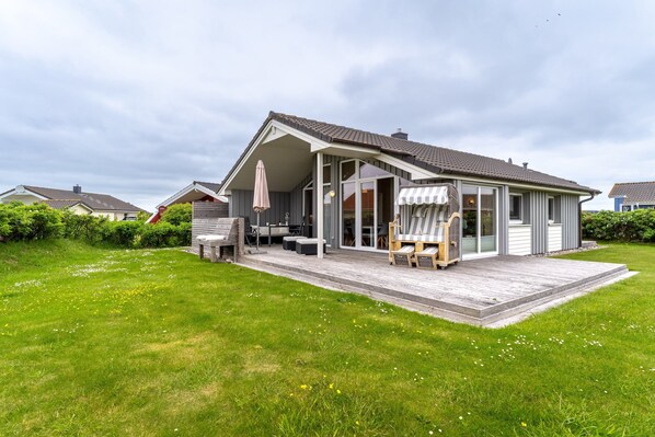 A modern house with a covered patio, a deck, and a lawn. - Holiday Home by North Sea With Sauna (Wesselburenerkoog)