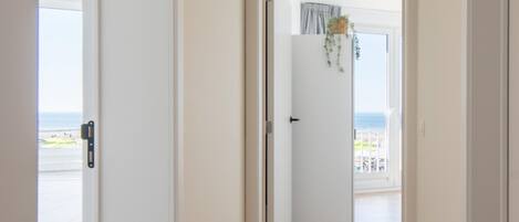 A hallway with wooden flooring leading to a door with a view of a balcony and beach.