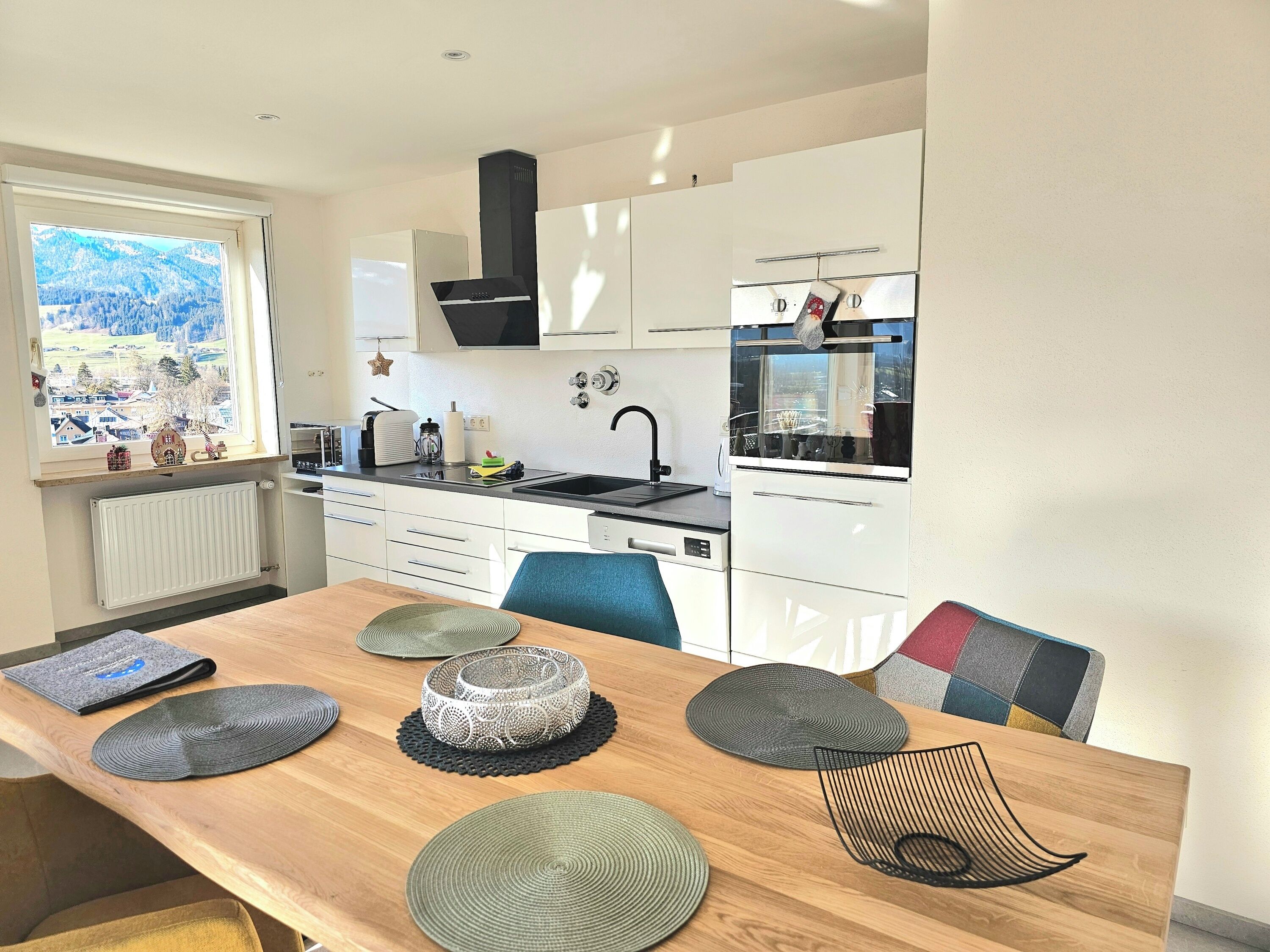 A modern kitchen with white cabinets, a black range hood, and a window with a view of a village.