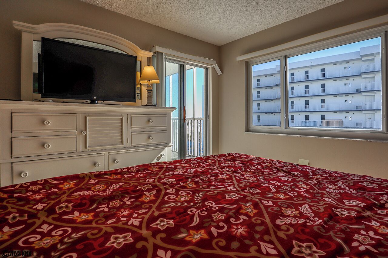 A bedroom with a large bed, a TV on a dresser, and a window with a view of a building.