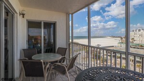 Un balcon avec une porte vitrée, une table ronde avec des chaises et une vue sur la plage et les bâtiments.
