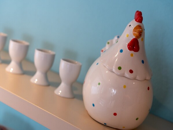 A ceramic chicken figurine with colorful polka dots on a shelf next to white ceramic cups. - Ferienhaus in Tonning (Toenning)