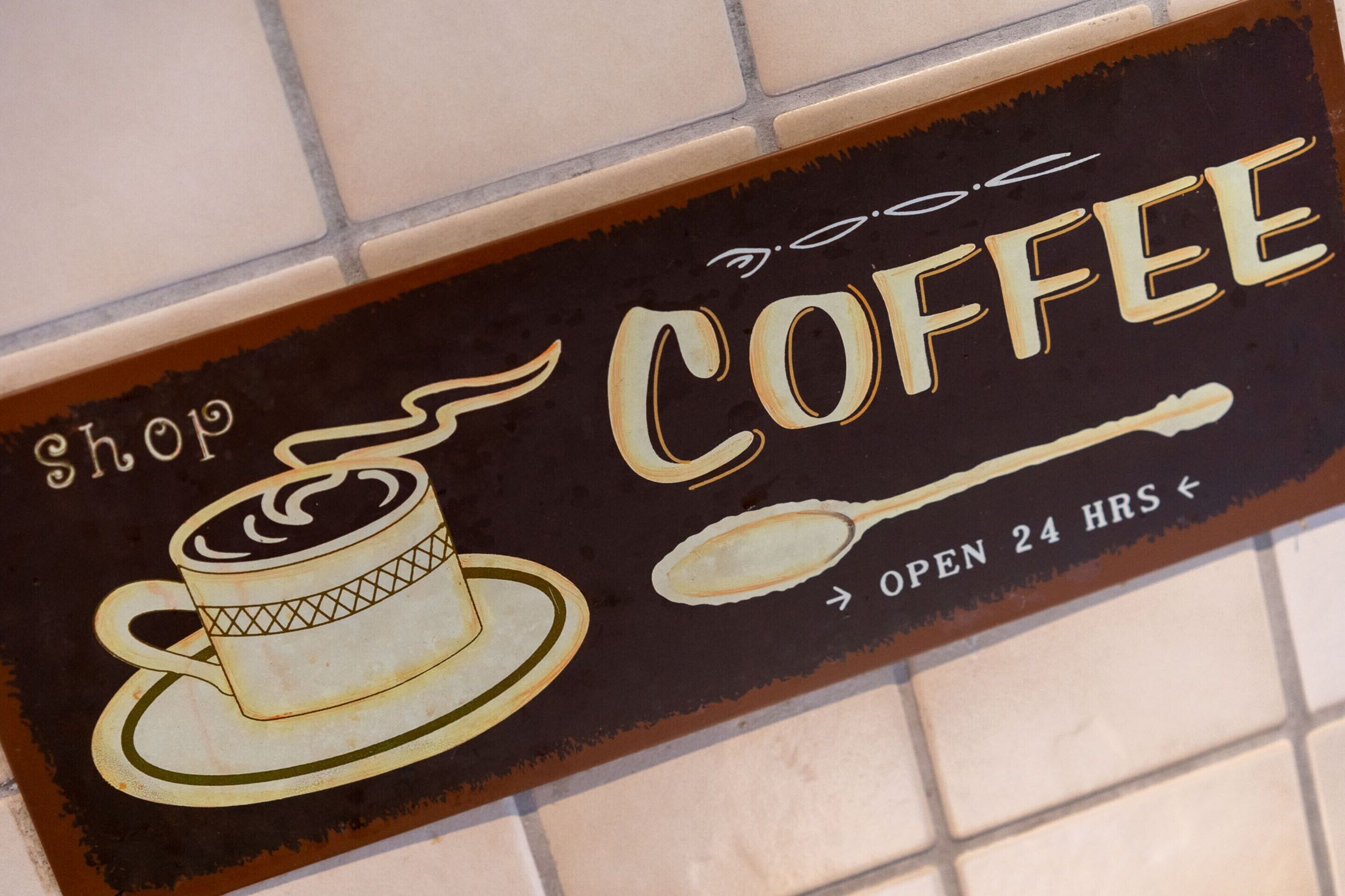 Skilt for en café med en kop kaffe og en ske, der angiver at den er åben døgnet rundt.