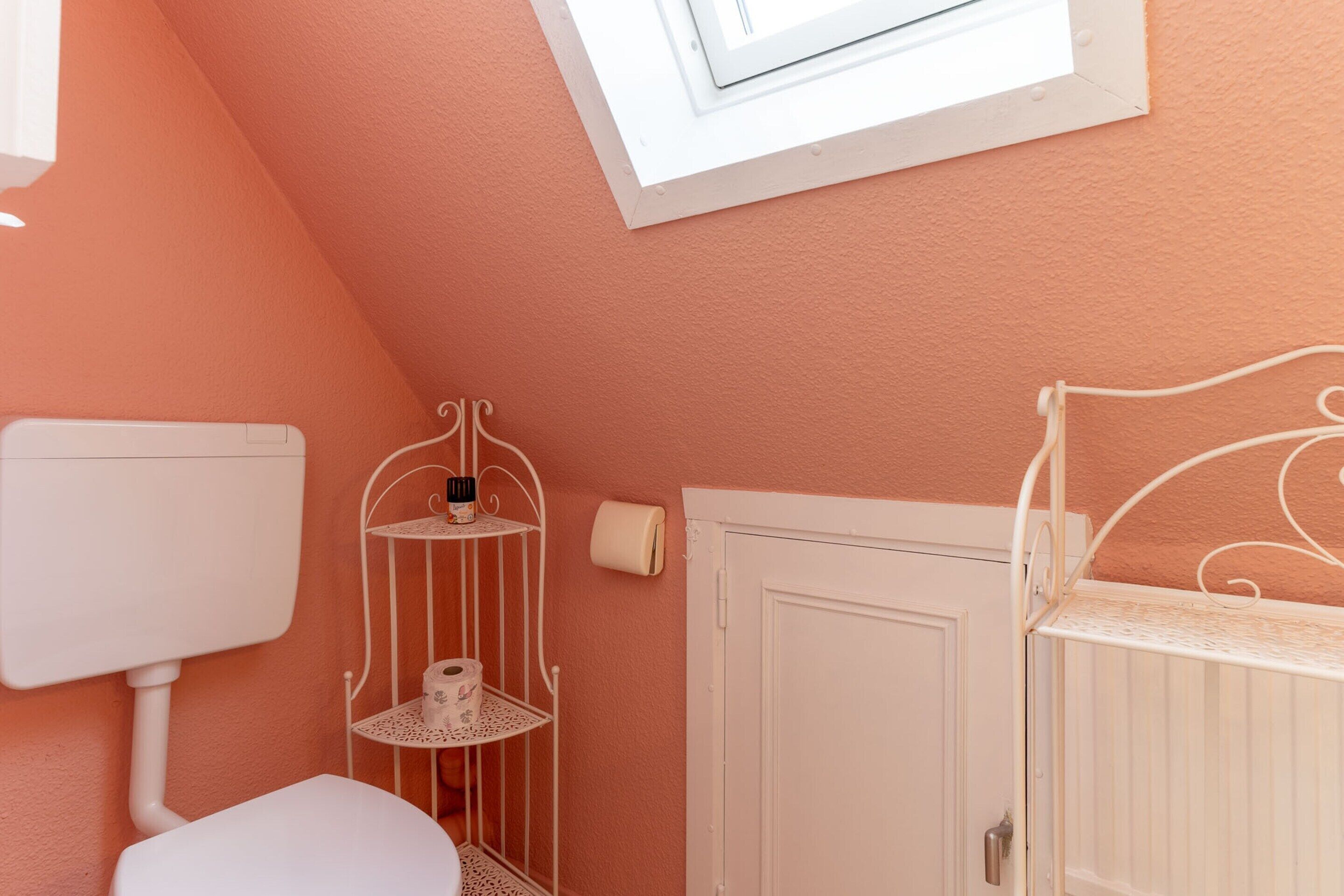 Ein Badezimmer mit Toilette, Handtuchheizkörper, Ablagefläche und Toilettenpapier sowie einer weißen Tür.