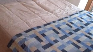 Een bed met een sprei, kussens en een houten hoofdbord.