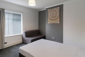 A bedroom with a bed, a sofa, a window with blinds, and a wall-mounted artwork. - Charming Algernon House in Warrington (Warrington)