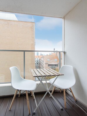 A balcony with two white chairs and a wooden table, overlooking a cityscape with brick buildings and a clear sky. - Modern Apartment in Ostend (Ostend)