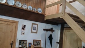 A wooden interior with a loft, wooden beams, a staircase, a wooden cabinet, a chair, and a table with a vase. - Gite Les Chavautes Rustic Style (Hamois)